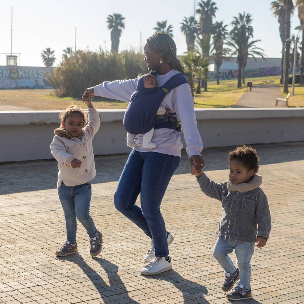 Woman walking with two children and a baby in a sling at a park.