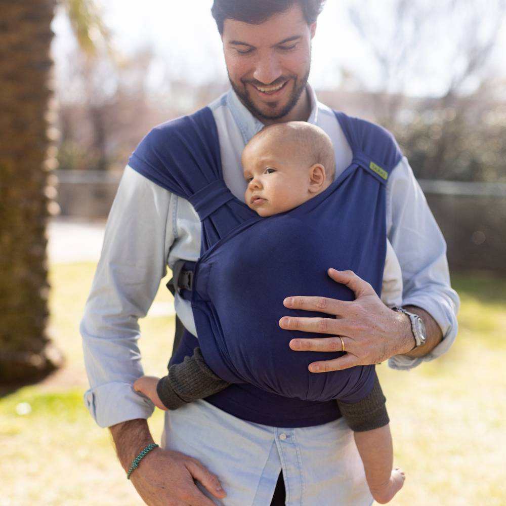Man holding a baby in a blue sling outdoors