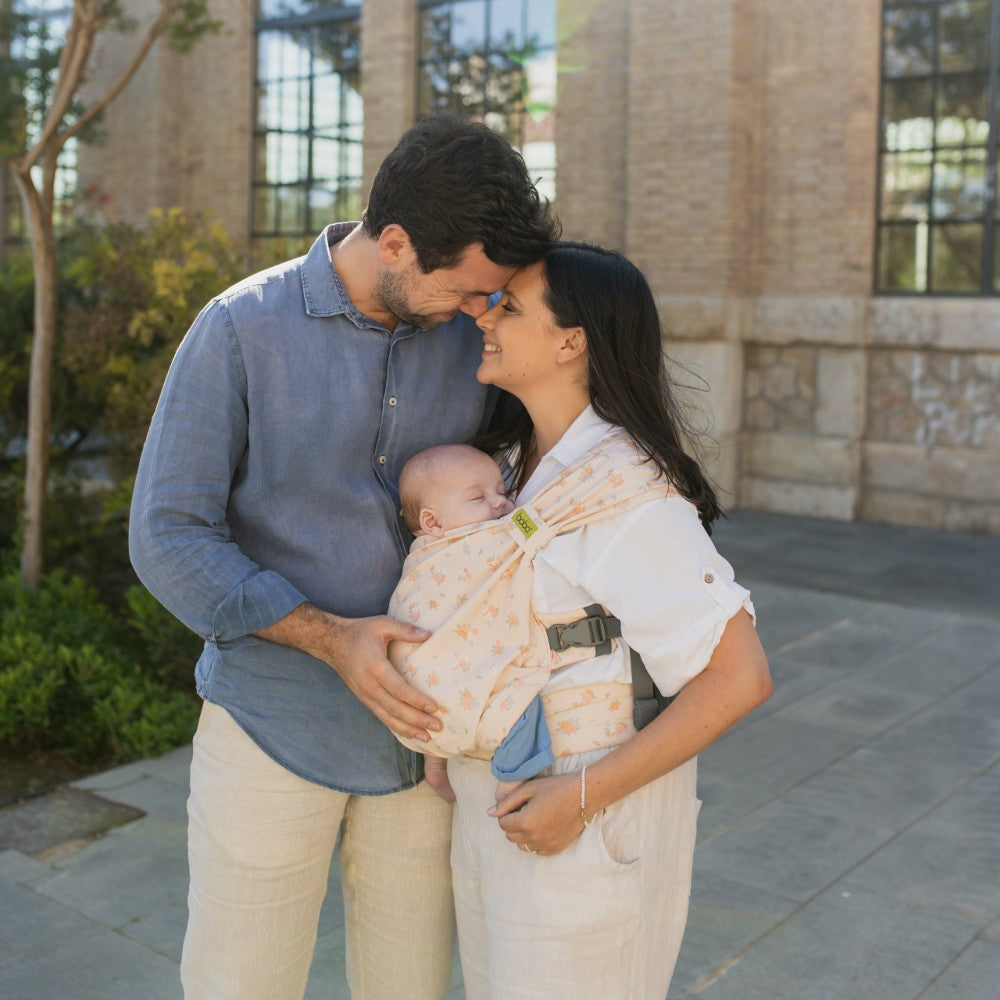 Man and woman holding a baby in a carrier outdoors.