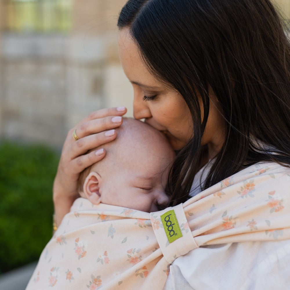 Woman kissing baby wrapped in a floral Boba baby carrier
