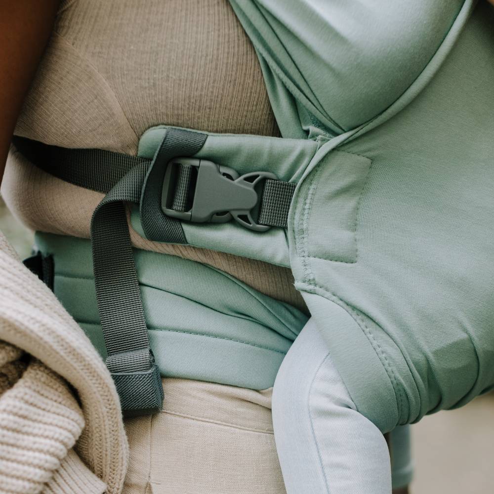 Close-up of a green baby carrier on a person wearing a beige sweater.