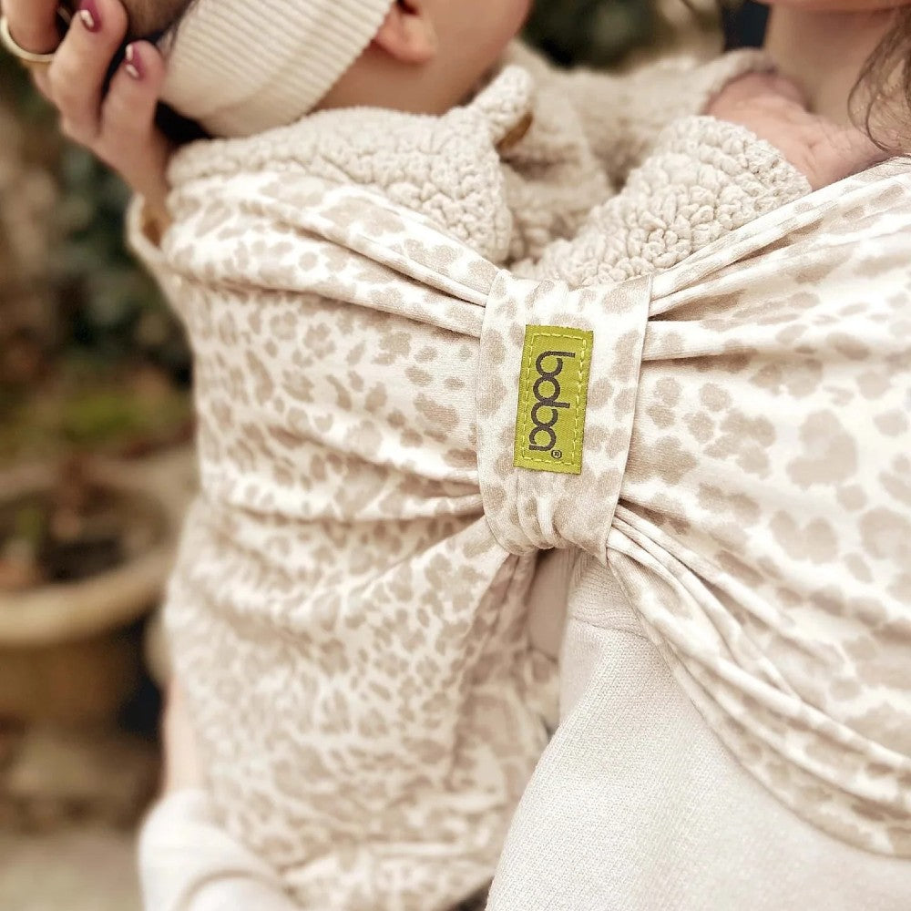 Close-up of a baby in Boba Bliss Leopard showing the safety loop, with a visible brand label, blurred background