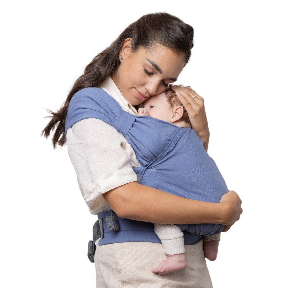 Woman holding a baby in a blue baby carrier against a white background