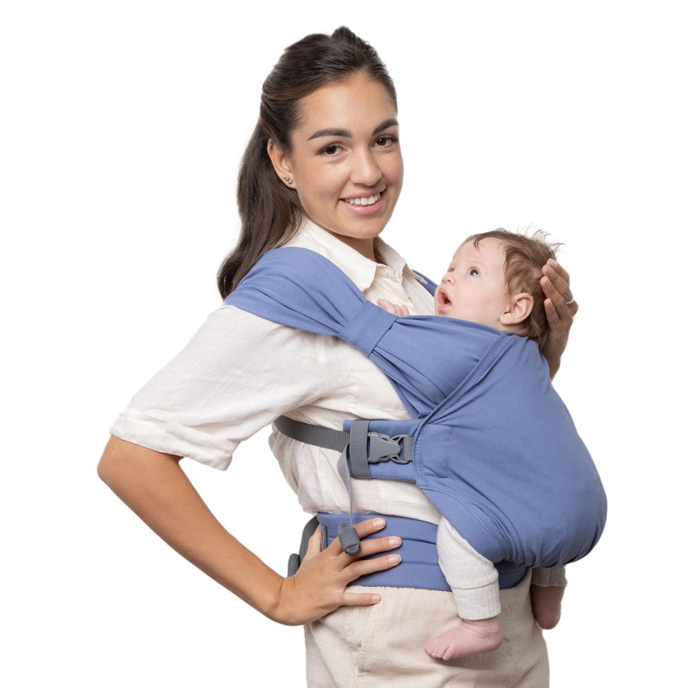 Woman holding a baby in a blue baby carrier against a white background