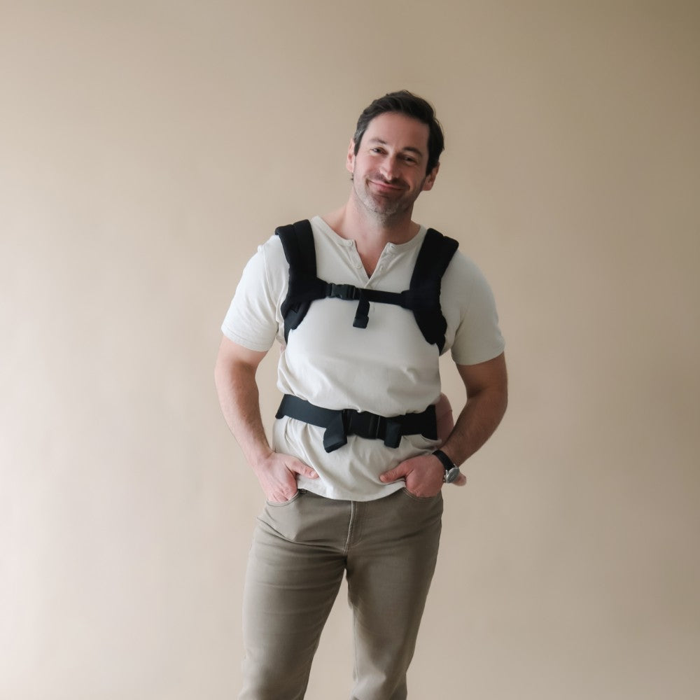 Man wearing a black baby carrier on his back on a beige background