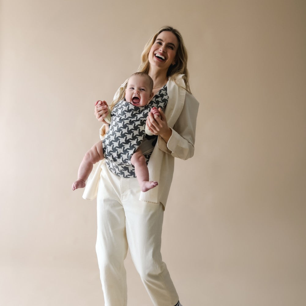 Woman holding a baby in a front-facing carrier against a plain background