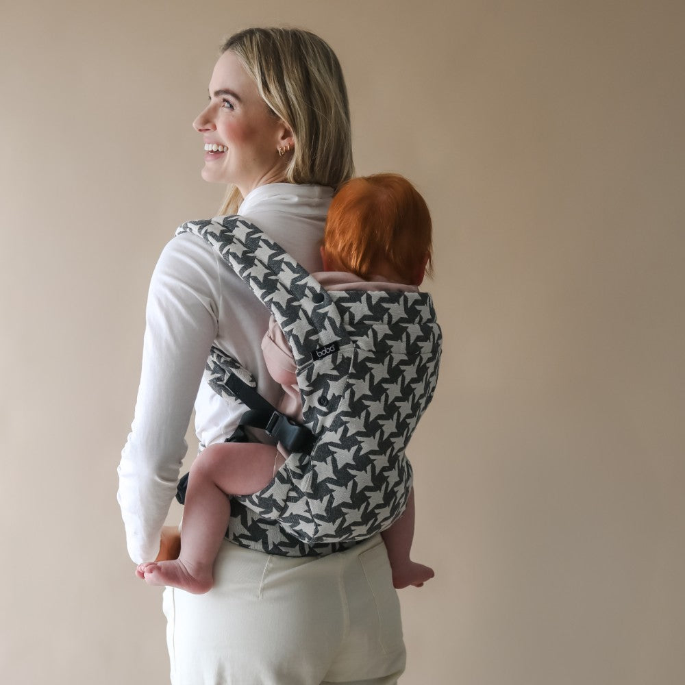 Woman carrying a baby in a patterned carrier against a plain background