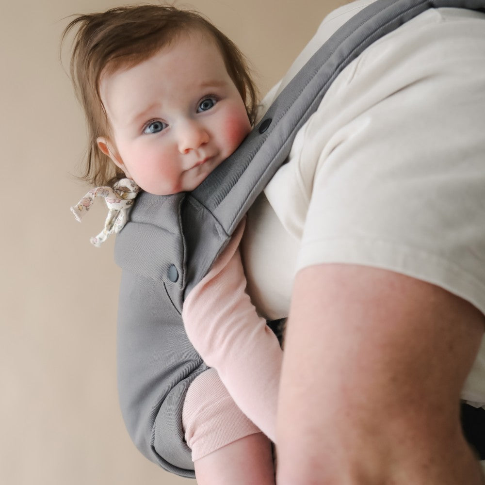 Baby worn on the back in a Boba Auri gray carrier with a neutral background