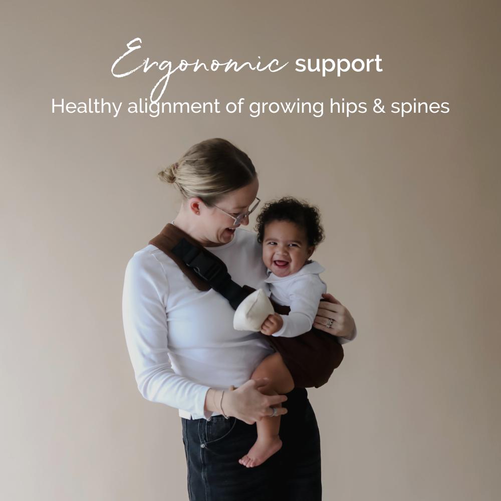 Woman holding a child using an ergonomic hip carrier with text about ergonomic support and healthy alignment.