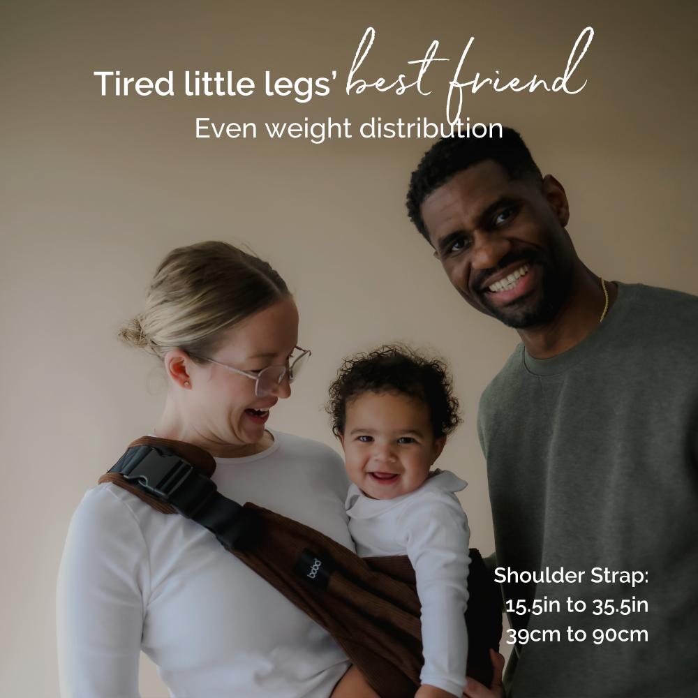 Family with a child in a carrier assist hip sling, smiling at the camera.