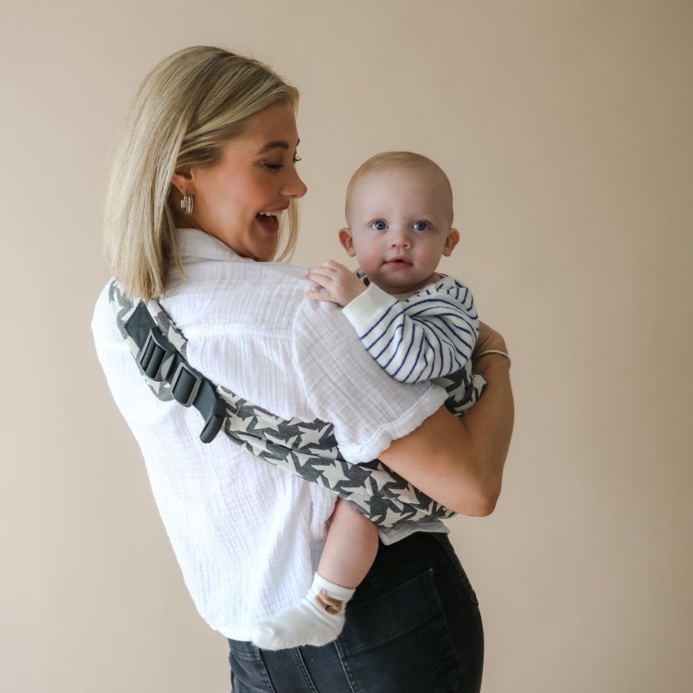 Woman holding a child in a toddler hip carrier against a beige background