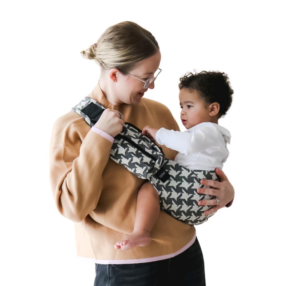Woman holding a baby in a patterned toddler hip carrier gainst a white background