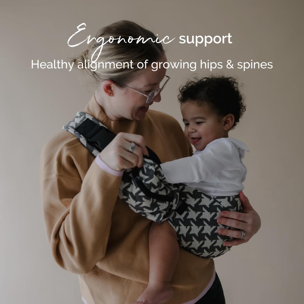 Woman holding a child in an ergonomic hip carrier with text about ergonomic support and healthy alignment.