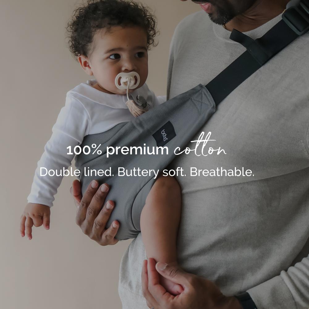 Child being carried in a gray hip carrier with text about premium cotton material.