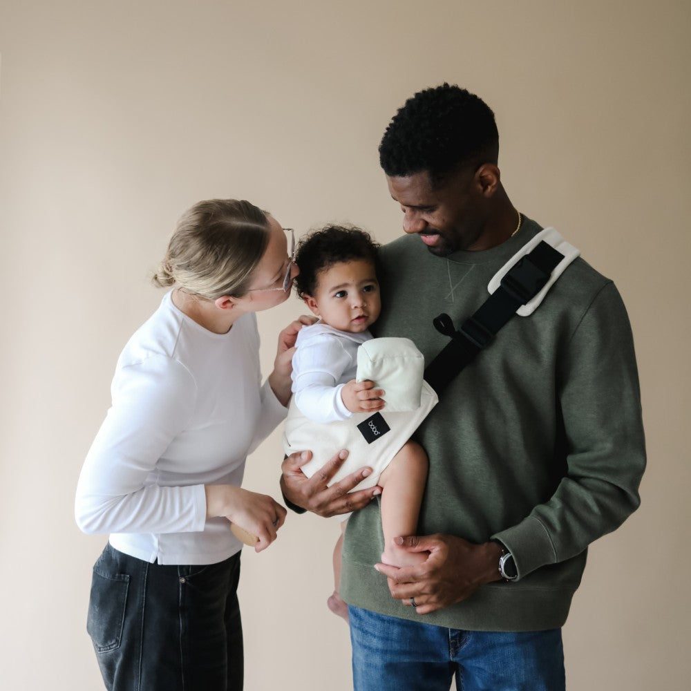 Family with a baby in a hip sling style carrier against a beige background