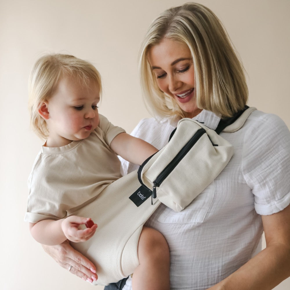 Woman holding a child using a toddler side sling carrier with a plain background