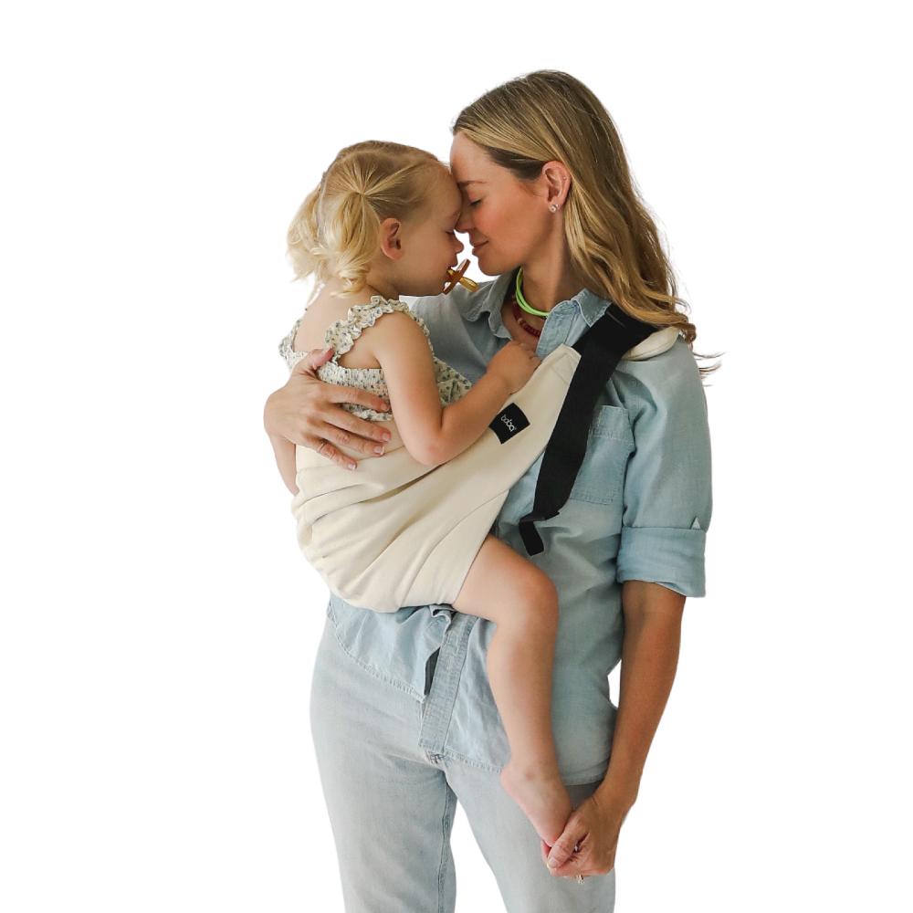 Woman holding a child in a baby hip sling carrier against a white background