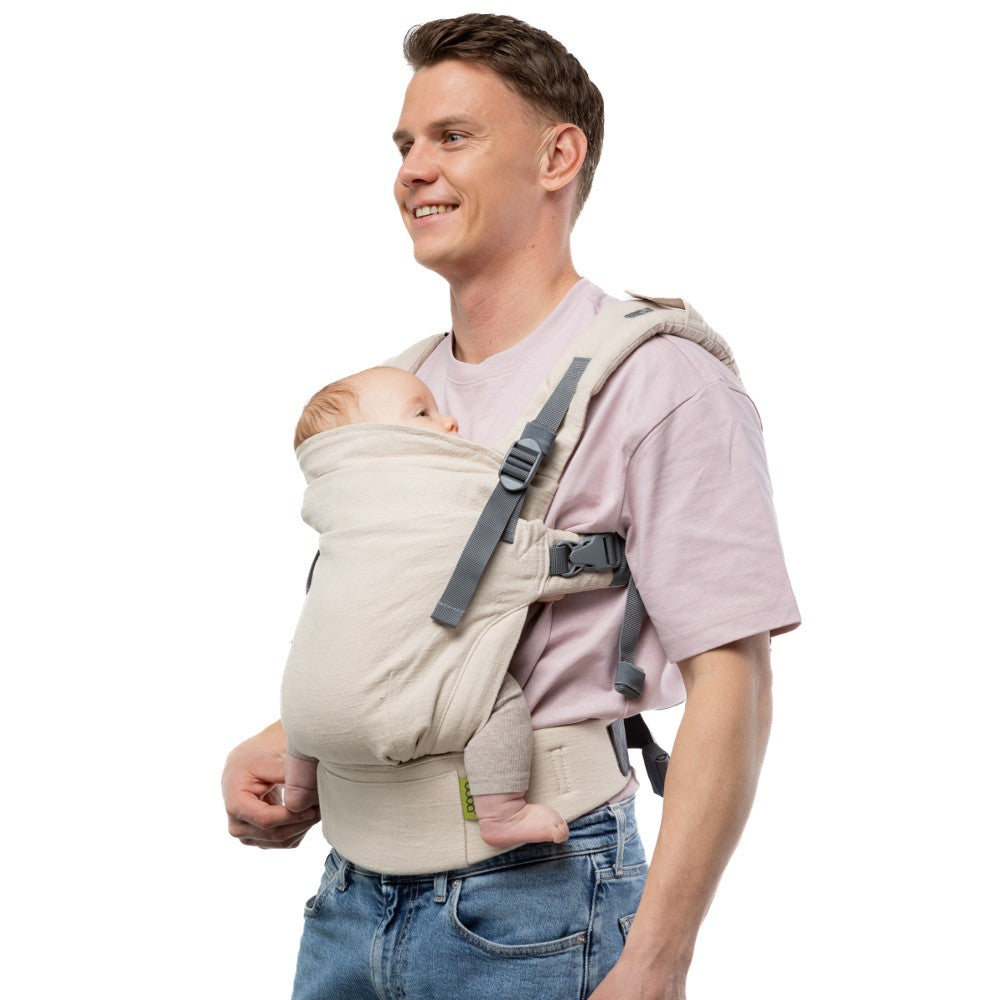 Man carrying a baby in a beige baby carrier against a white background