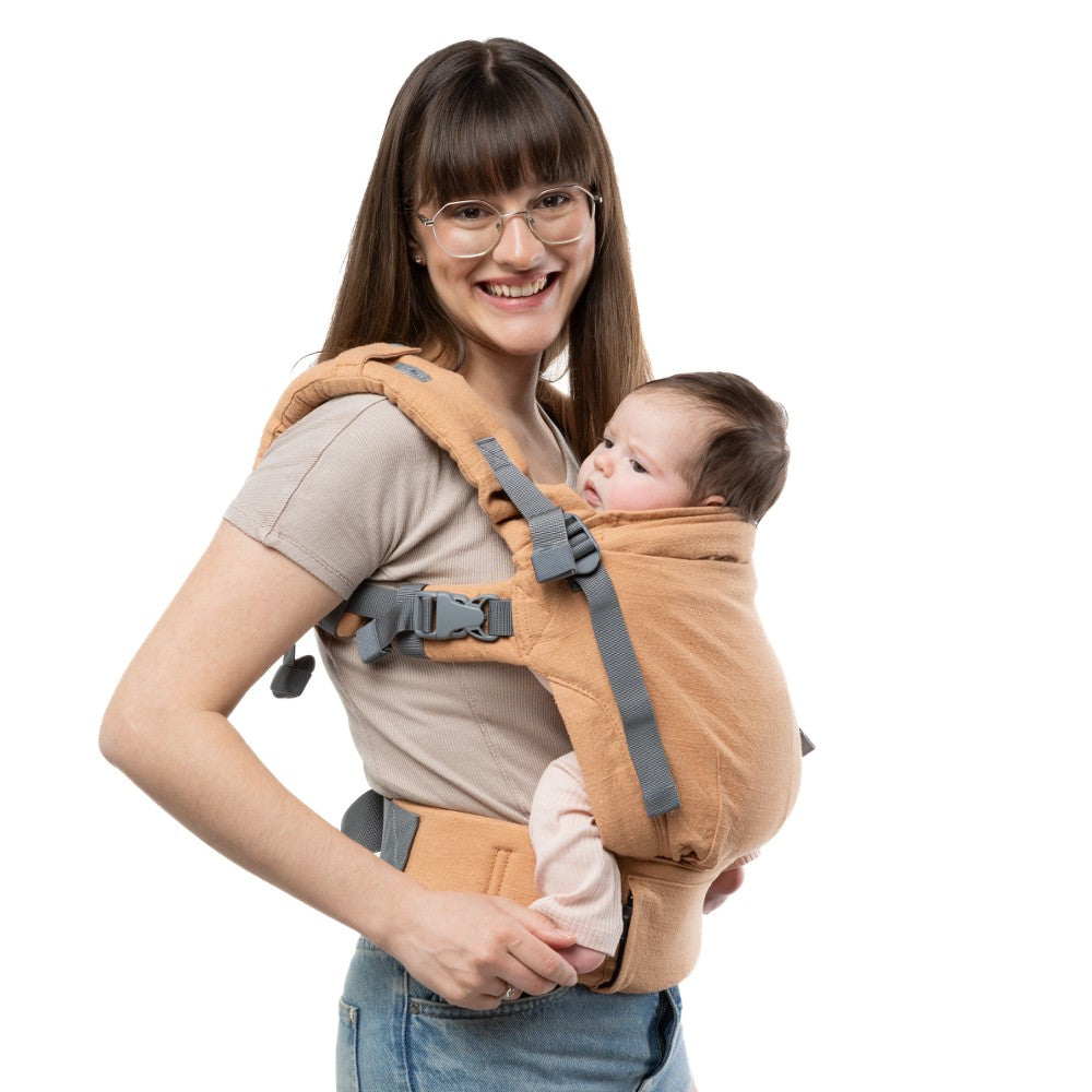 Woman carrying a baby in a rust brown linen baby carrier on a white background