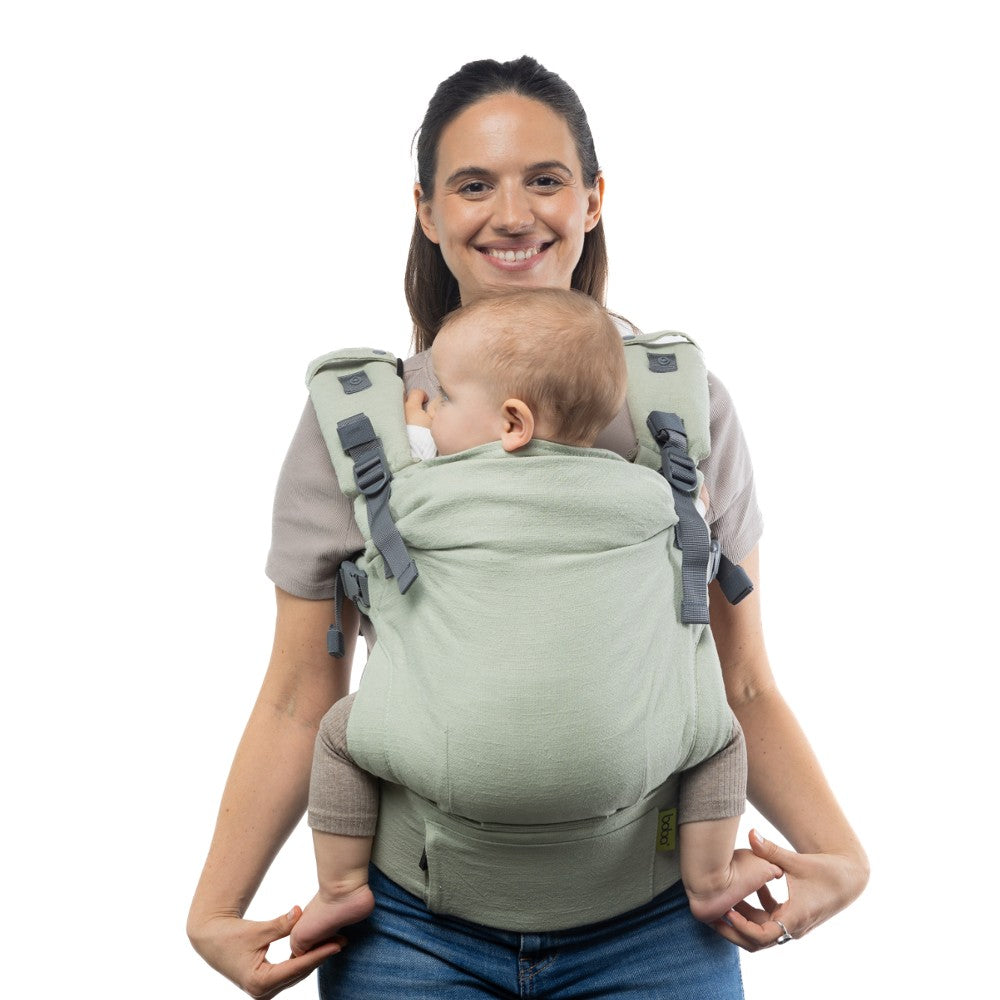 Woman carrying a baby in a green baby carrier against a white background