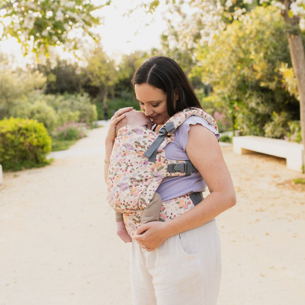 Woman carrying a baby in a floral baby carrier outdoors.