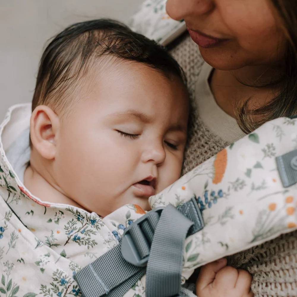 Baby in a floral-patterned carrier with a person holding it, set against a neutral background.