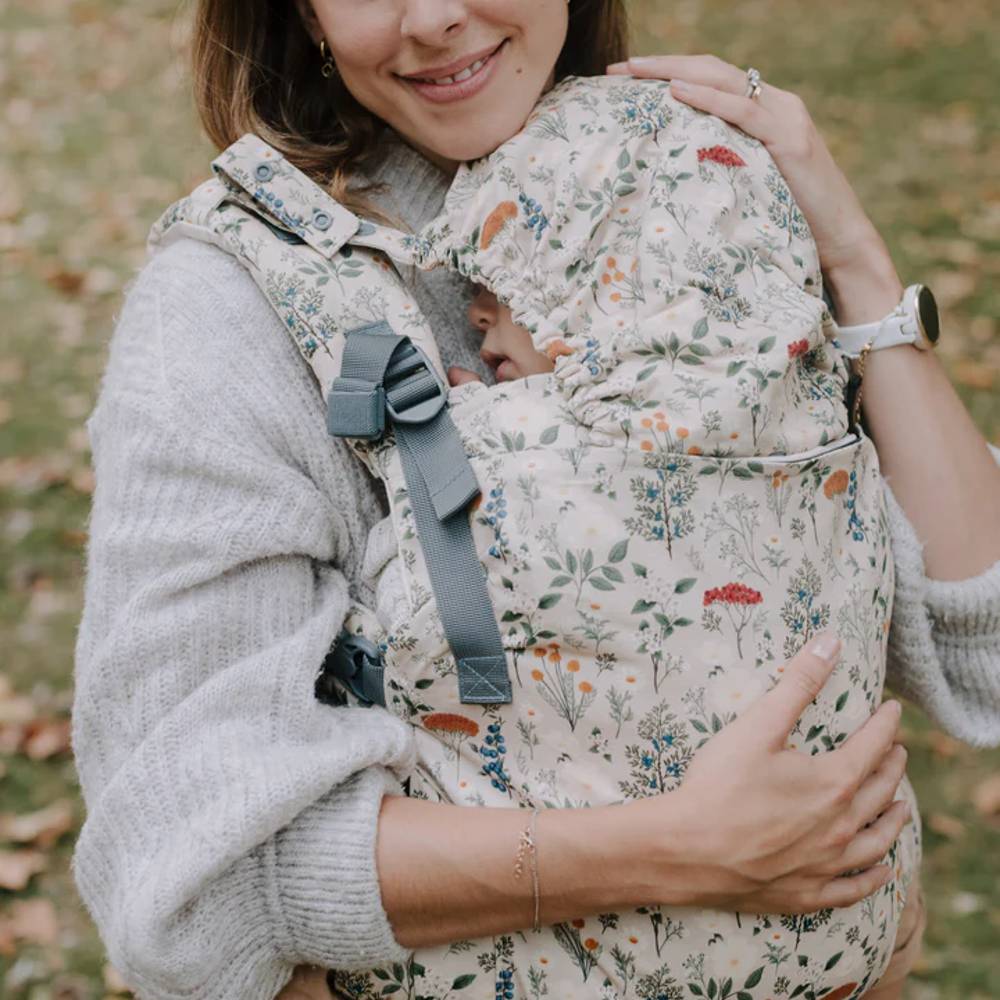Woman holding a baby in a floral-patterned carrier outdoors.