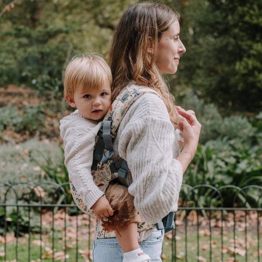 Woman carrying a child on her back ina  beautiful floral Boba X baby carrier through a park