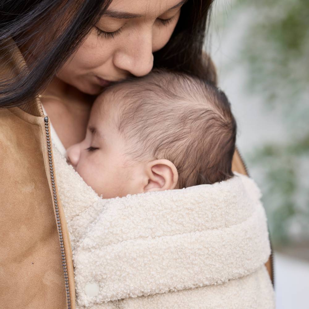 Woman holding a baby wrapped in a boucle beige fashion on trend baby carrier Boba Auri Teddy style