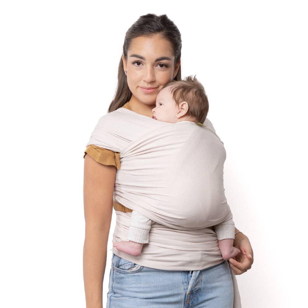 Woman holding a baby in a beige wrap carrier against a white background