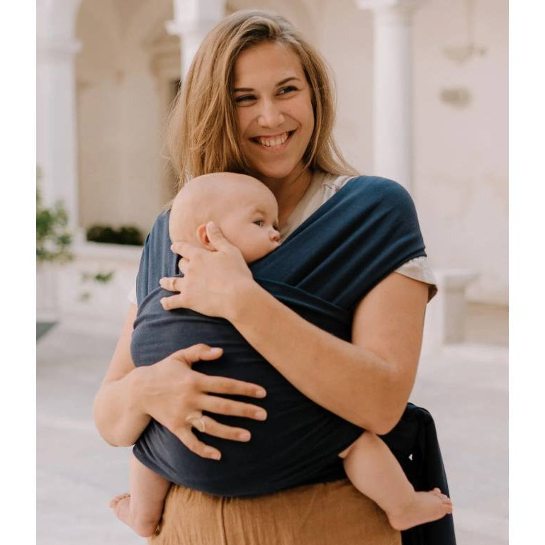 Woman holding a baby in a sling outdoors with arches in the background