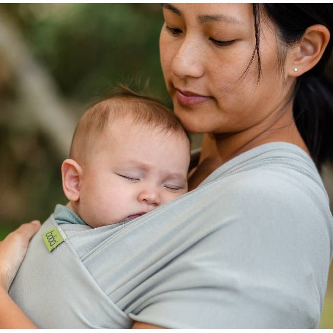 Woman holding a baby in a sling outdoors