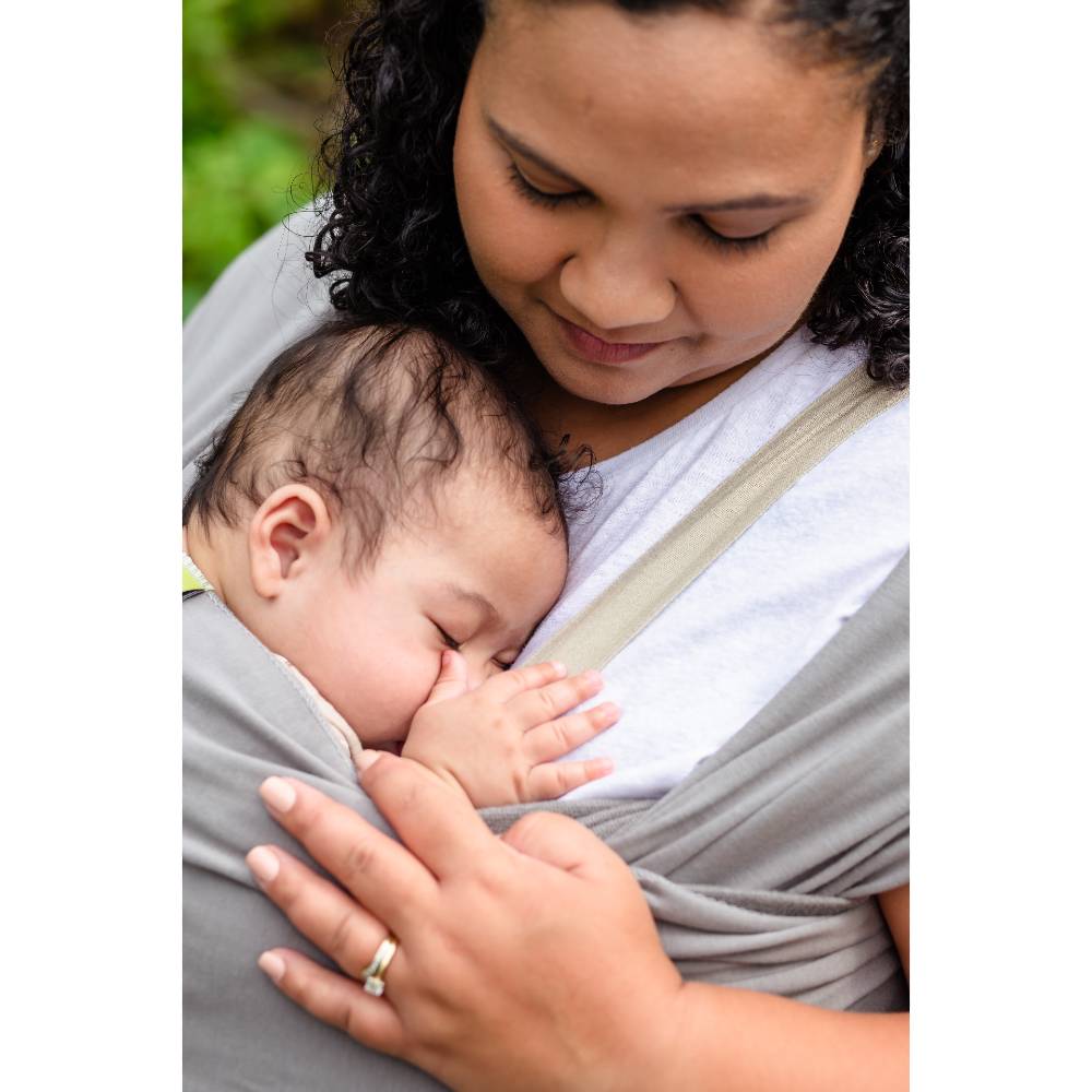 Woman holding a baby in a sling with a blurred green background