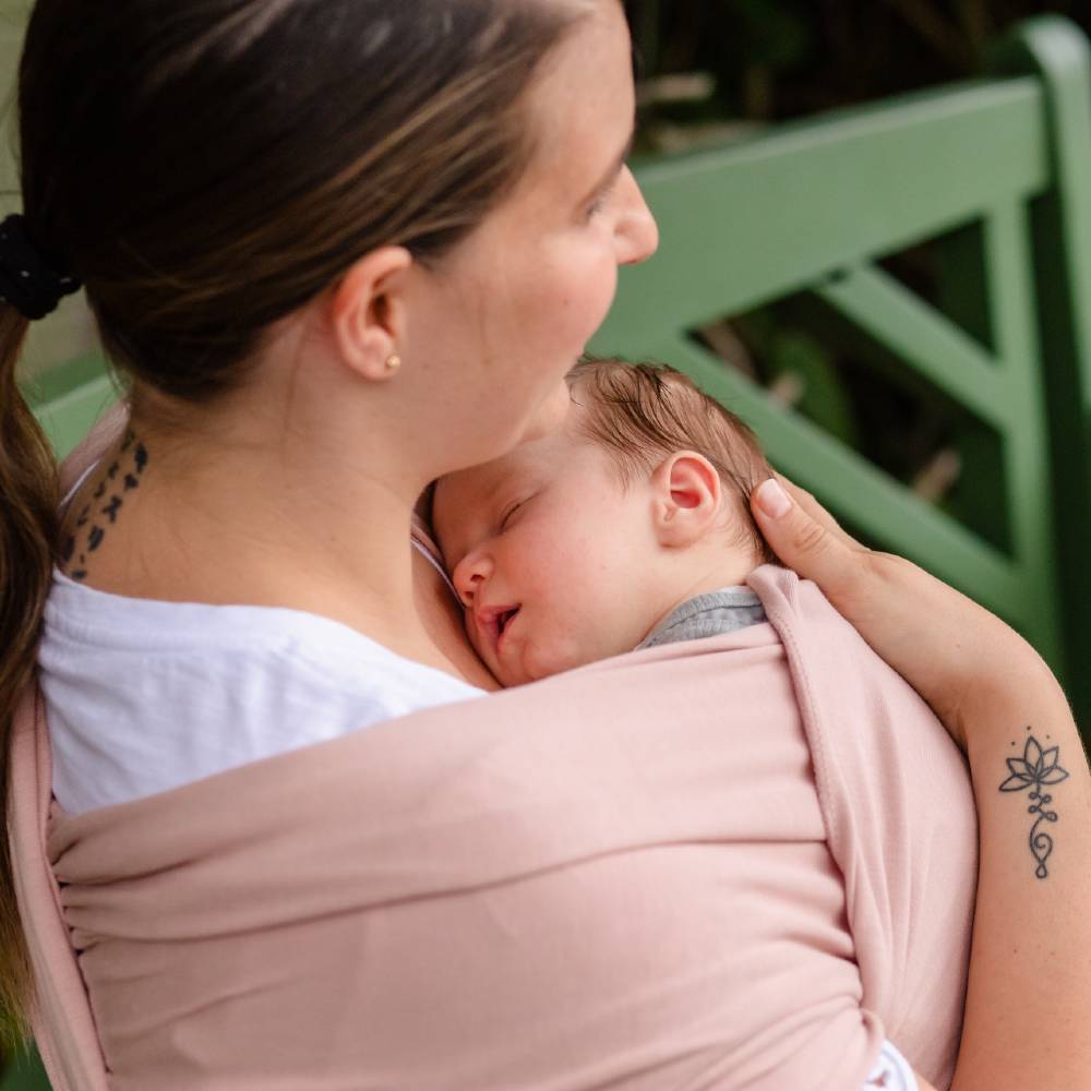 Woman holding a baby in a pink Boba wrap sling outdoors