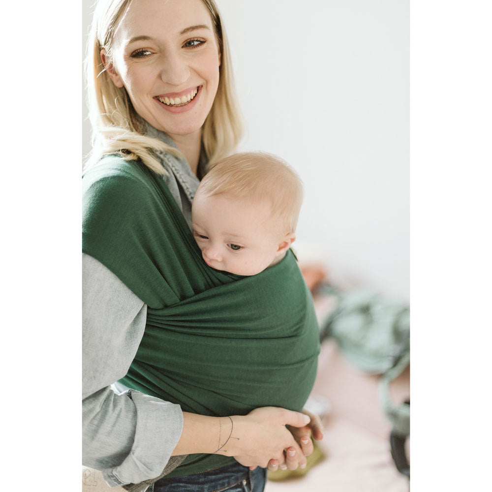 Woman holding a baby in a green stretchy wrap against a white background