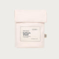 A pale blush pink cotton bottom sheet in a folded pouch package, featuring a white rectangular label with black text that reads 'babu basics. bottom sheet' and '100% organic cotton'.