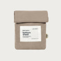 A folded beige cotton bottom sheet with a white paper label reading 'bubu basics. bottom sheet' and a small side tag, photographed on a light gray background.