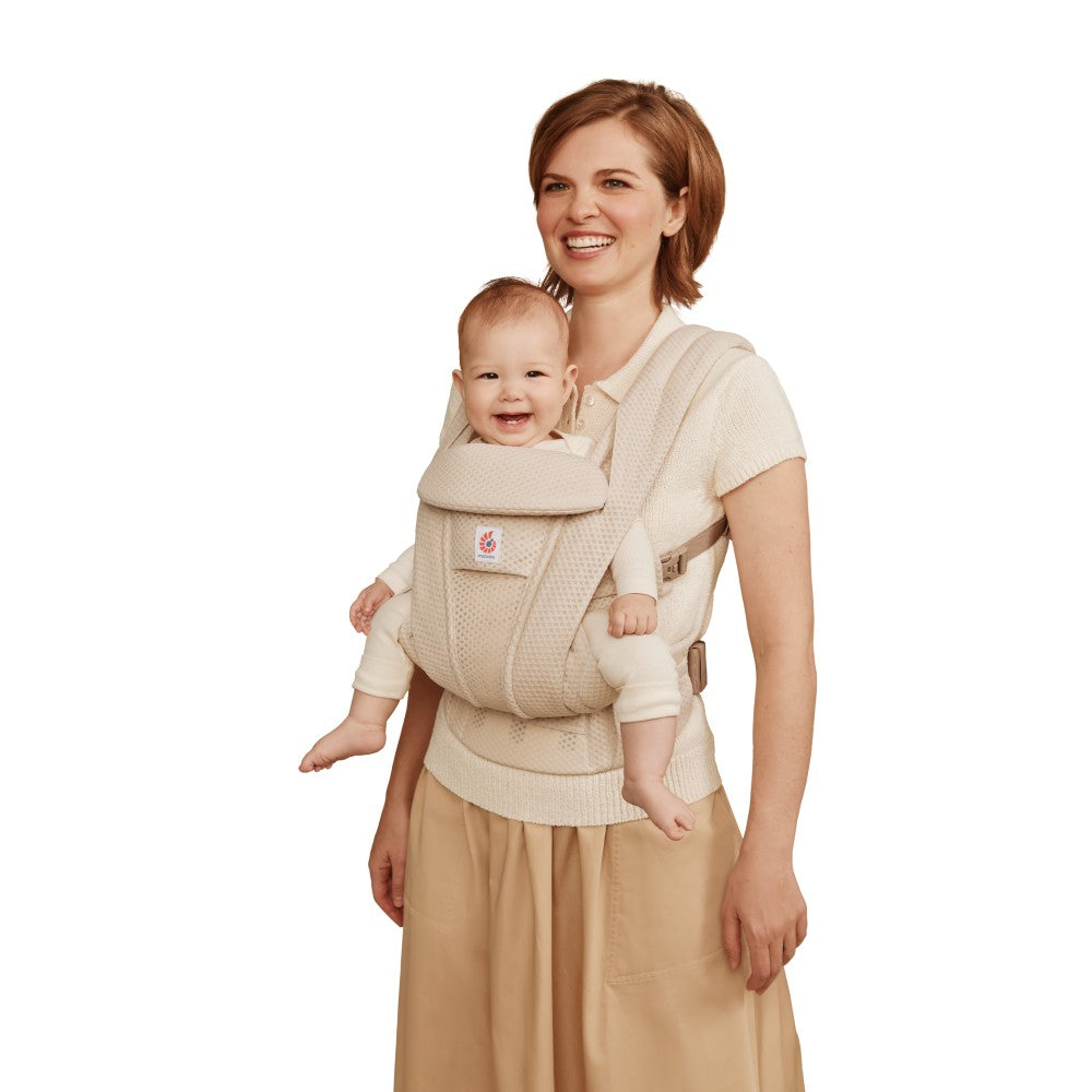Woman holding a baby in a beige baby carrier against a white background