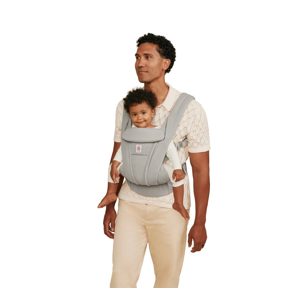 Man holding a baby in a gray baby carrier against a white background