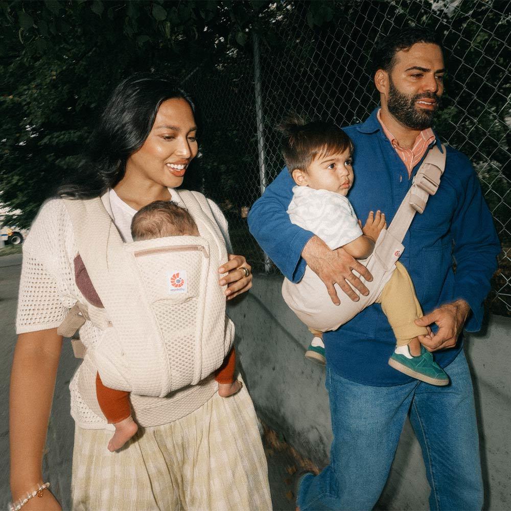 Two adults walking outdoors with children in baby carriers.