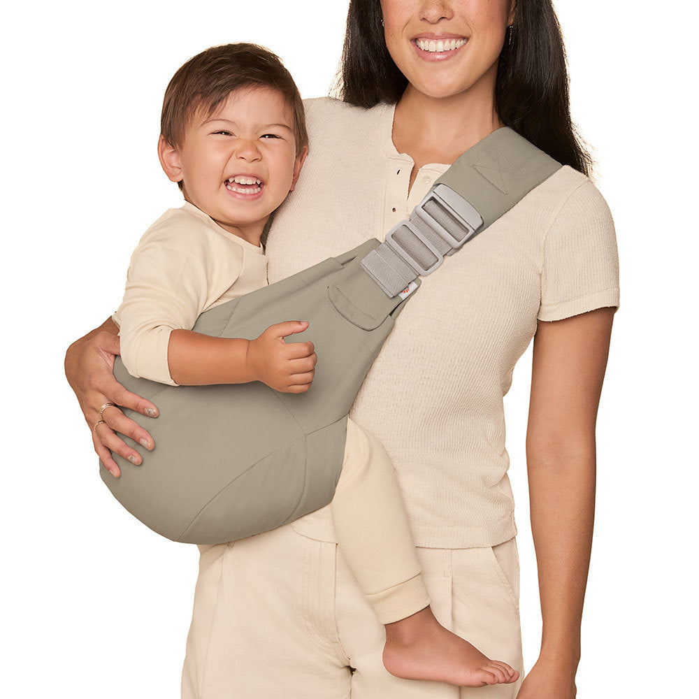 Woman carrying a child in a Olive green toddler hip carrier with a strap on a white background