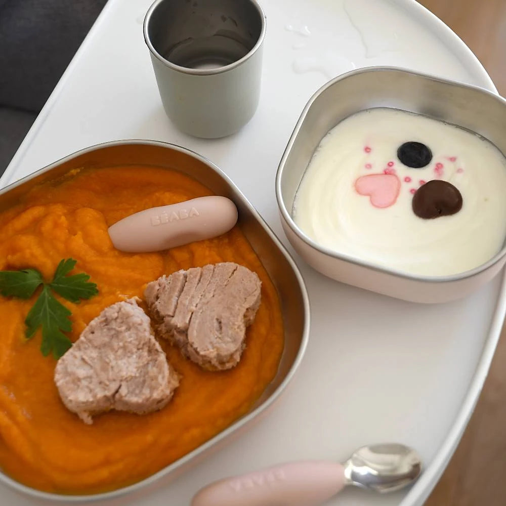 Stainless steel flatware set in pink colour with pumpkin soup and fish on the plate and yoghurts and blueberries in the bowl 