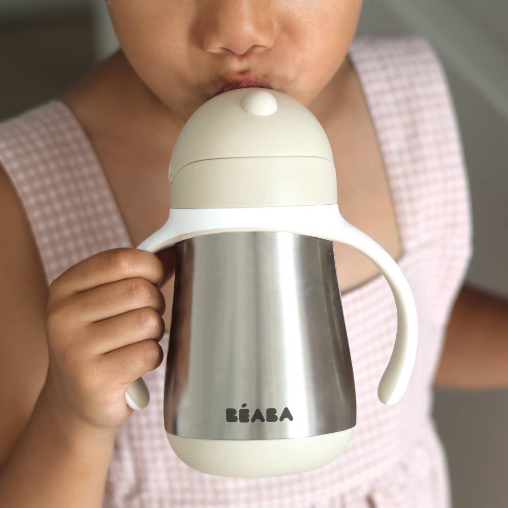 A close-up of a child drinking from a stainless steel handled sipper bottle with a beige lid. The brand name 'BEBABA' is printed on the front.