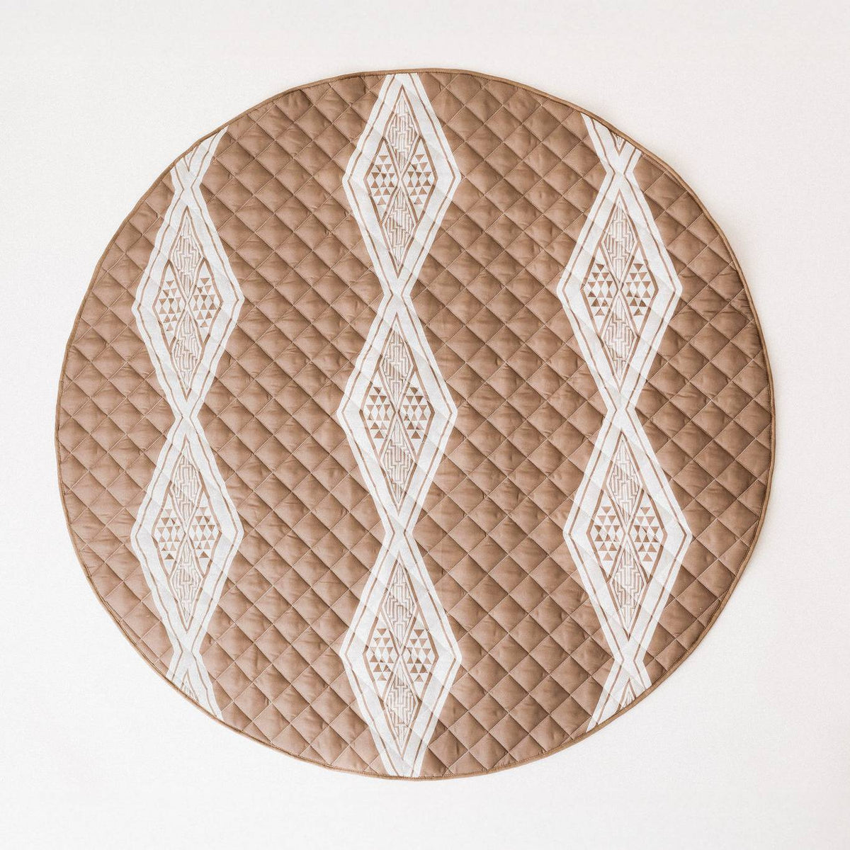 A brown circle quilted playmat with a maori insrpired design on a natural colour background. 