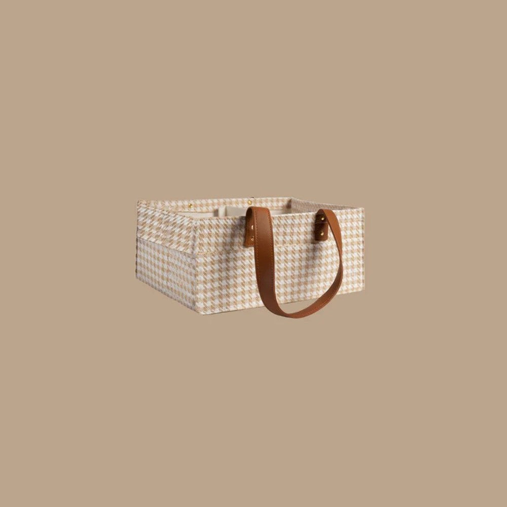 A rectangular storage basket with a beige and white houndstooth pattern, featuring two brown leather handles, set against a solid beige background.