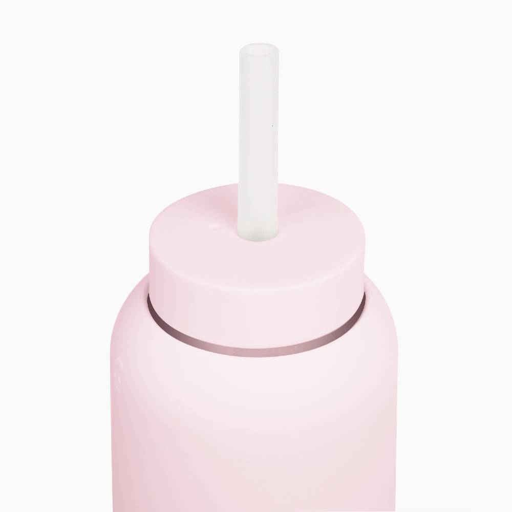 A close-up of a matte light pink bottle with a matching pink lid and a white cylindrical straw, set against a solid white background.