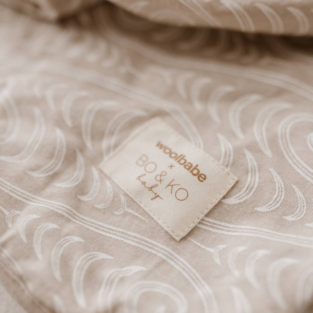 Close-up of a beige patterned fabric with a sewn-in label reading 'woolbabe x BO & KO baby'.