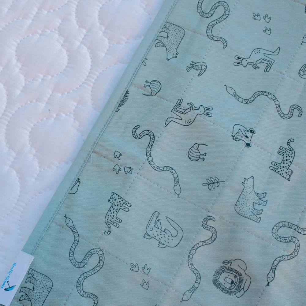 A close-up of a quilted brolly sheet with a light mint green background and a black line art animal pattern, laid next to a white quilted mattress protector