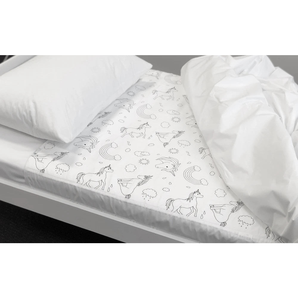 A white quilted brolly sheet with a black line-art unicorn and rainbow pattern is shown on a bed, with a white pillow and white duvet cover.