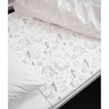 A white quilted brolly sheet mattress protector with a black line-art unicorn and rainbow pattern, shown partially pulled down over a bed with white bedding.